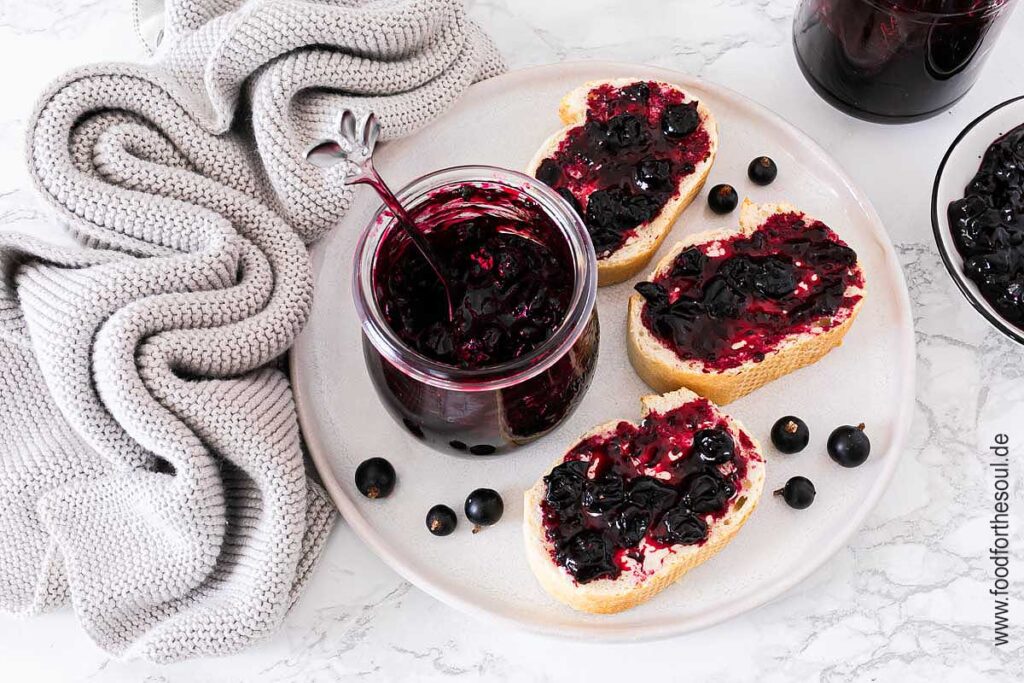 Selbstgemachte Johannisbeermarmelade in einem Glas und auf Baguettescheiben