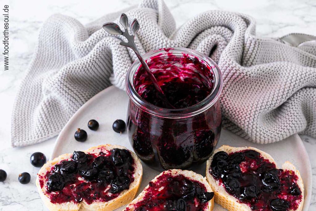 Selbstgemachte Johannisbeermarmelade in einem Glas und auf Baguettescheiben