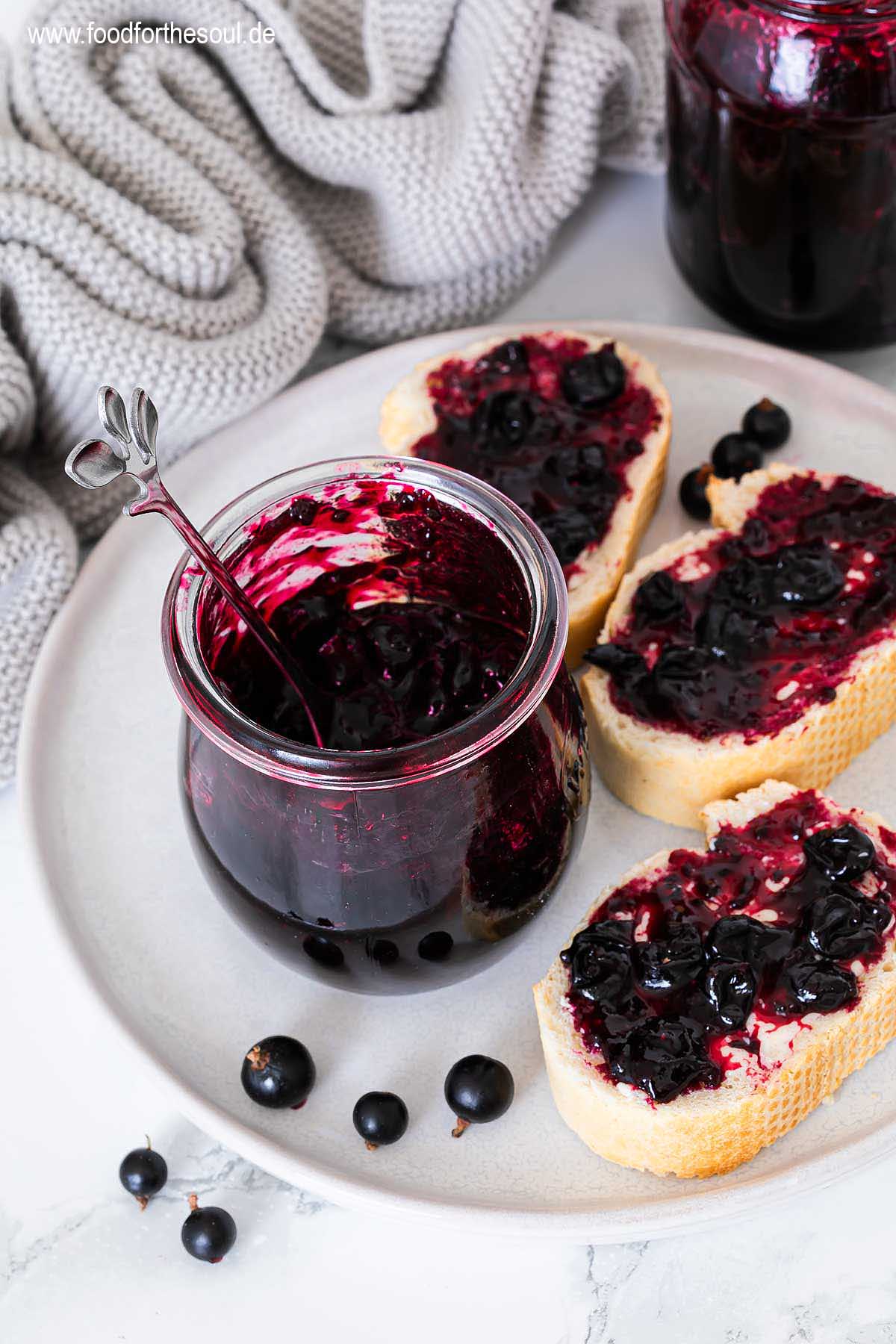 Selbstgemachte Johannisbeermarmelade in einem Glas und auf Baguettescheiben