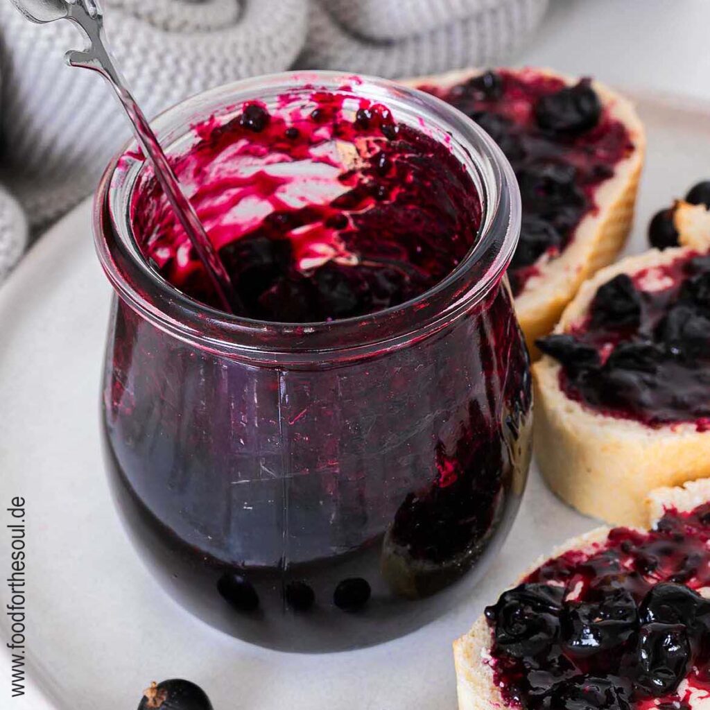 Selbstgemachte Johannisbeermarmelade in einem Glas und auf Baguettescheiben