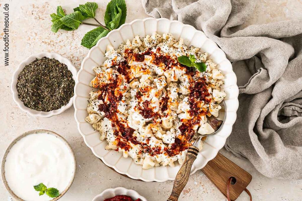 Frisch gekochte türkische Manti mit Joghurtsauce und Tomaten-Paprikabutter auf einem Teller
