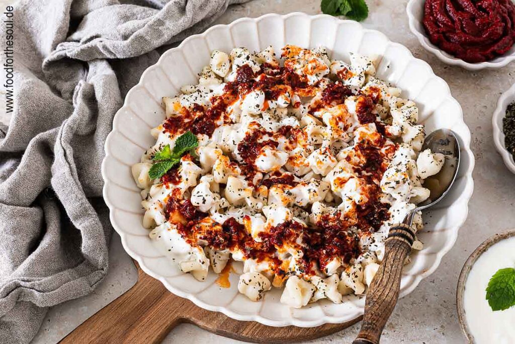 Frisch gekochte türkische Manti mit Joghurtsauce und Tomaten-Paprikabutter auf einem Teller