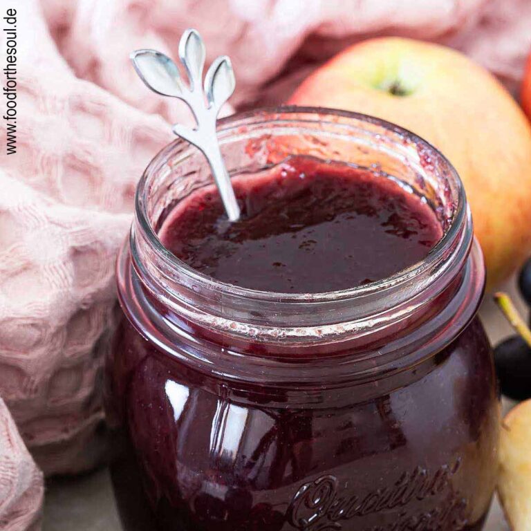 Ein Glas mit frisch gekochter Apfel-Trauben-Marmelade neben Weintrauben und Äpfeln