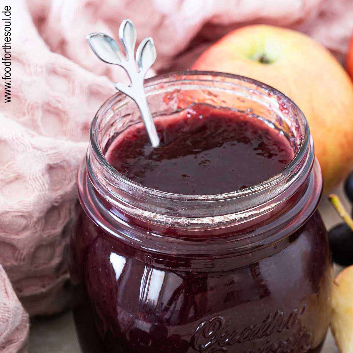 Ein Glas mit frisch gekochter Apfel-Trauben-Marmelade neben Weintrauben und Äpfeln